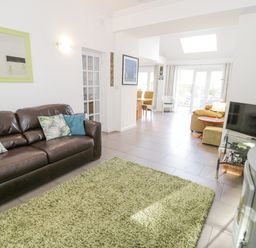 A living room with a leather sofa and green rug next to a TV and dining area at Mountain View in Conwy