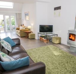 A living room with two sofas a television on a stand a wood stove and glass doors leading outside at Mountain View in Conwy