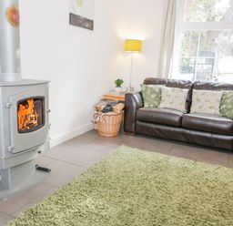 A room with a wood burning stove a brown leather sofa with patterned cushions a green rug and a floor lamp at Mountain View in Conwy