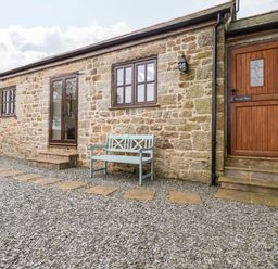 Exterior view of a stone building with wooden door and windows and a bench on a gravel path at Brocks Barn Sweetshouse near Lostwithiel