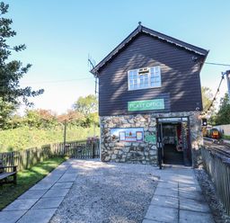 An outdoor ticket office building next to railway tracks with a bench and a fenced path at The Station Flat in St Newlyn East near Newquay