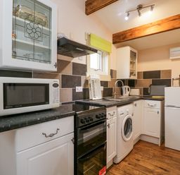 A kitchen with white cabinets black countertop microwave oven washing machine small refrigerator and wooden floor at The Log Cabin in Bushton near Royal Wootton Bassett