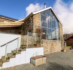 An exterior view of a stone building with large windows a staircase with glass railing and planters at The Barn at Glanoer Hundred House near Builth Wells