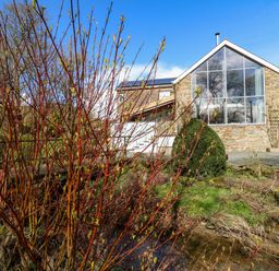 A stone house with large windows and a garden with bushes and a small stream at The Barn at Glanoer Hundred House near Builth Wells