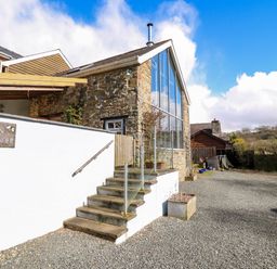 The exterior of a stone barn with large glass windows and steps leading to a white wall at The Barn at Glanoer Hundred House near Builth Wells