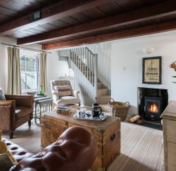 A living room with wooden beams a fireplace leather and fabric chairs a chest coffee table and a staircase at Thimble Cottage in Mevagissey