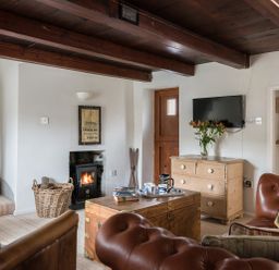 A living room with wooden beams leather chairs a wood stove and a wooden chest at Thimble Cottage in Mevagissey