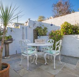 An outdoor patio with a white metal table and chairs surrounded by potted plants and flowers at Thimble Cottage in Mevagissey