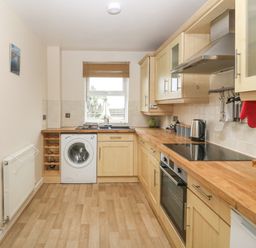 A kitchen with wooden cabinets and countertops a washing machine an oven a stove and a window at Beach View in Benllech near Red Wharf Bay