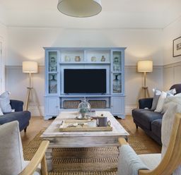 A living room with sofas a wooden coffee table a blue entertainment unit and two standing lamps at Ty Carmel in Rhosneigr