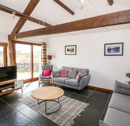 A living room with grey sofas a round wooden coffee table a tv on a stand and large windows at Y Beudy in Criccieth