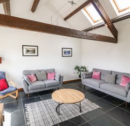 A living room with grey sofas pink and black cushions wooden beams and skylights at Y Beudy in Criccieth