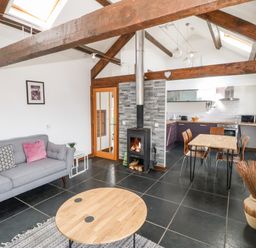 An open plan living room and kitchen with a fireplace and wooden beams at Y Beudy in Criccieth