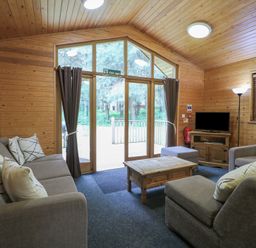 A living room with a sofa set, wooden coffee table, television on a cabinet, and large glass doors at Birch Lodge in Rosliston