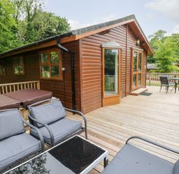An outdoor wooden deck with seating area and hot tub next to a wood cabin at The Beeches in Narberth