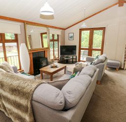 A living room with two grey sofas a wooden coffee table a television and large windows at The Beeches in Narberth