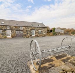 A stone building with multiple windows and doors on a large gravel area with metal farm equipment at Ysgybor Yd in Chwilog near Criccieth