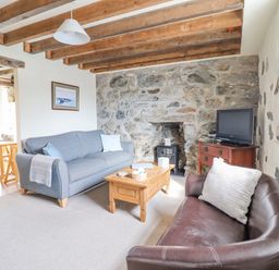 A living room with a blue sofa brown chair wooden coffee table and a television at Ysgybor Yd in Chwilog near Criccieth