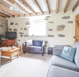 A living room with exposed wooden beams stone walls a gray sofa a brown leather loveseat a wooden coffee table and a television at Ysgybor Yd in Chwilog near Criccieth