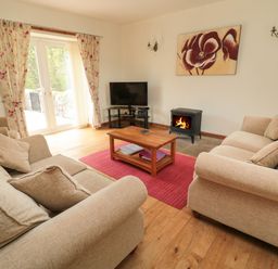 A living room with two beige sofas a wooden coffee table a red rug a wood stove and a television at Gardeners Cottage in Belford near Bamburgh