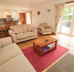 A living room with beige sofas a wooden coffee table on a red rug and a kitchen area in the background at Gardeners Cottage in Belford near Bamburgh