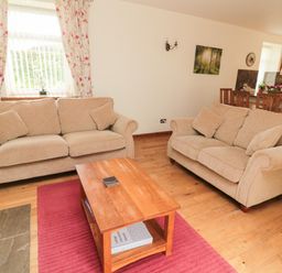 A living room with two beige sofas and a wooden coffee table on a red rug at Gardener's Cottage Belford near Bamburgh