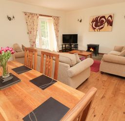 A living room with sofas a television a fireplace and a dining table with flowers at Gardener's Cottage Belford near Bamburgh