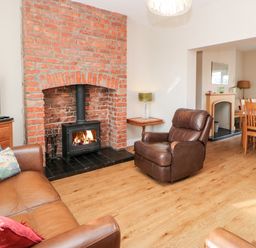 A living room with a brick fireplace leather chairs a wooden dining table and a television at Lightkeeper House in Amble-by-the-Sea