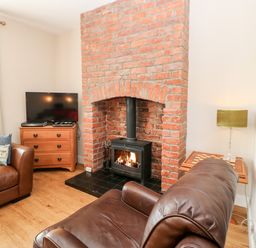 A living room with a brick fireplace a wood stove leather sofas a TV on a wooden cabinet and a side table with a lamp at Lightkeeper House in Amble-by-the-Sea