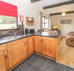 A kitchen with wooden cabinets and a black countertop open to a living room with three brown recliner chairs and a television at Bluebell Lodge in Saltburn-by-the-Sea