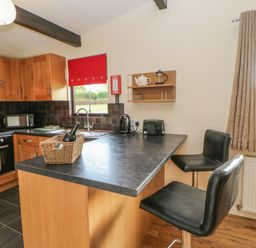 A kitchen with a countertop, two black bar stools, cabinets, oven, microwave, and window at Bluebell Lodge in Saltburn-by-the-Sea