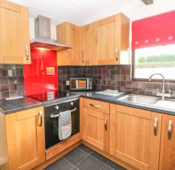 A kitchen with wooden cabinets black countertop black tiled backsplash and a red window blind at Bluebell Lodge Saltburn-by-the-Sea