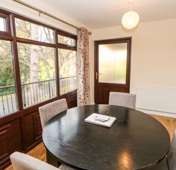 A dining room with a round black table four chairs large windows and a wooden door at Violet Lodge in Saltburn-by-the-Sea