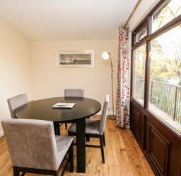A dining room with a round black table and four chairs next to large windows at Violet Lodge in Saltburn-by-the-Sea