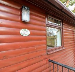 Exterior view of a wooden cottage wall with a window a light fixture and a sign saying violet cottage at Violet Lodge in Saltburn-by-the-Sea