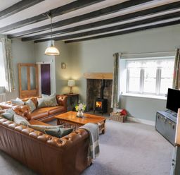 A living room with leather sofas a wooden coffee table a wood burning stove and a television at Beck Cottage in Pickering