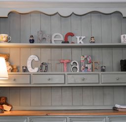 A wooden cabinet with shelves holding decorative letters spelling Beck Cottage a lamp on the left and books on the right