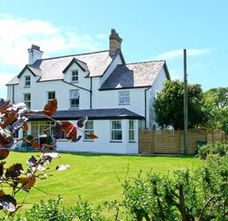 A white multi-story house with a slate roof and garden at Carreg Rhys in Malltraeth near Newborough