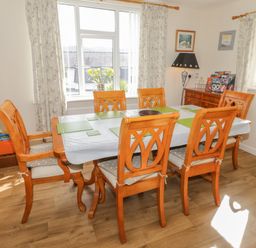 A dining room with wooden table and six chairs near windows with curtains at Bangor Cottage in Bangor