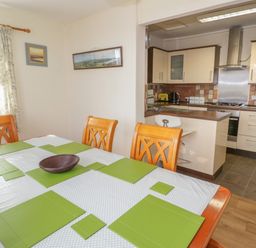 A dining area with a table set with placemats and a bowl adjacent to an open kitchen with cabinets and appliances at Bangor Cottage in Bangor