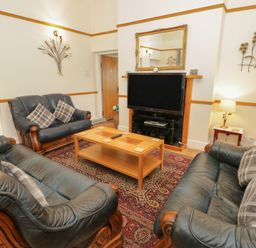 A living room with three leather sofas a wooden coffee table a large television on a stand a patterned rug and wall decorations at Bangor Cottage in Bangor