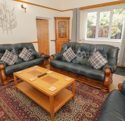 A living room with black leather sofas a wooden coffee table and a patterned carpet at Bangor Cottage in Bangor