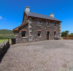 A stone house with multiple windows and chimneys surrounded by grass and hills at Brandon Holiday Home in Cloghane County Kerry