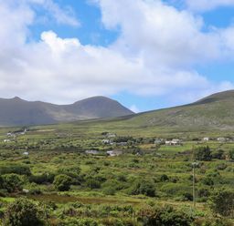 A green rural landscape with hills houses and a partly cloudy sky at Brandon Holiday Home in Cloghane County Kerry