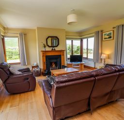 A living room with brown leather sofas a wooden fireplace and a television at Brandon Holiday Home in Cloghane County Kerry