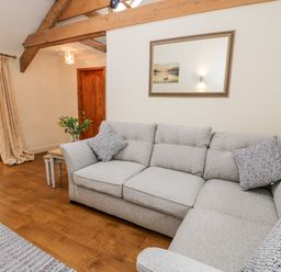 A living room with a gray sofa wooden floor a wooden door and exposed ceiling beams at Ty Taid in Llanddaniel Fab near Beaumaris