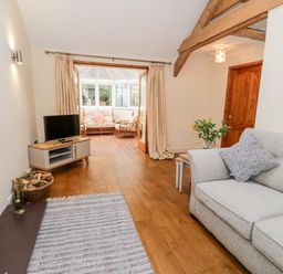 A living room with a gray sofa a TV on a stand a wood burning stove and double doors leading to a sunroom at Ty Taid in Llanddaniel Fab near Beaumaris