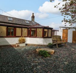 A garden with a wooden bench and gravel at Ty Taid in Llanddaniel Fab near Beaumaris