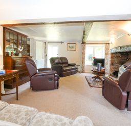 A living room with leather recliners a wooden cabinet a brick fireplace and a small round table with a television at Lyons Green in Little Fransham near Swaffham