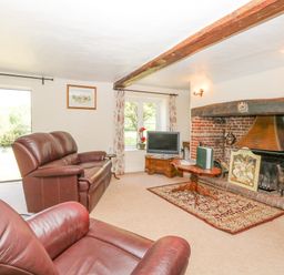 A living room with leather sofas a TV on a wooden stand a fireplace and a rug at Lyons Green in Little Fransham near Swaffham
